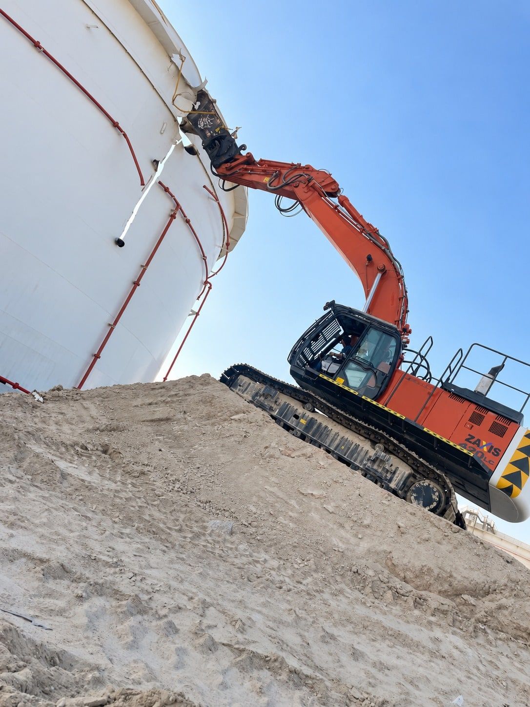 Excavator on an earth ramp cutting into the shell of a storage tank