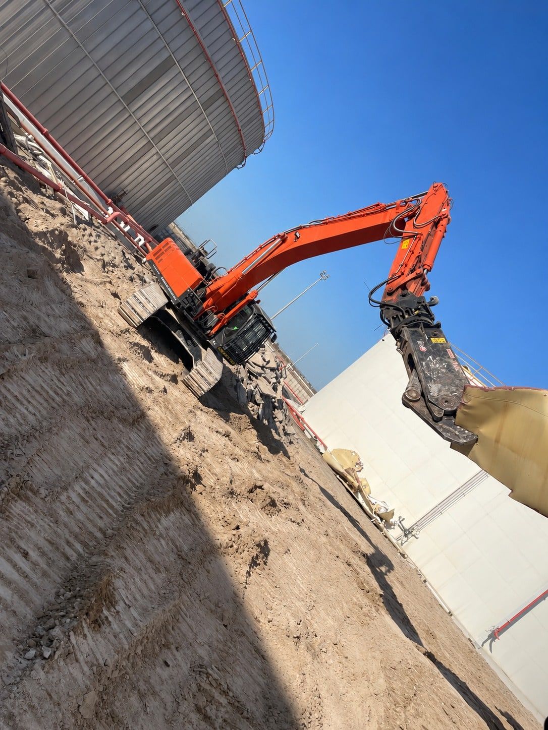 Excavator with shear cutting the shell plates of a storage tank
